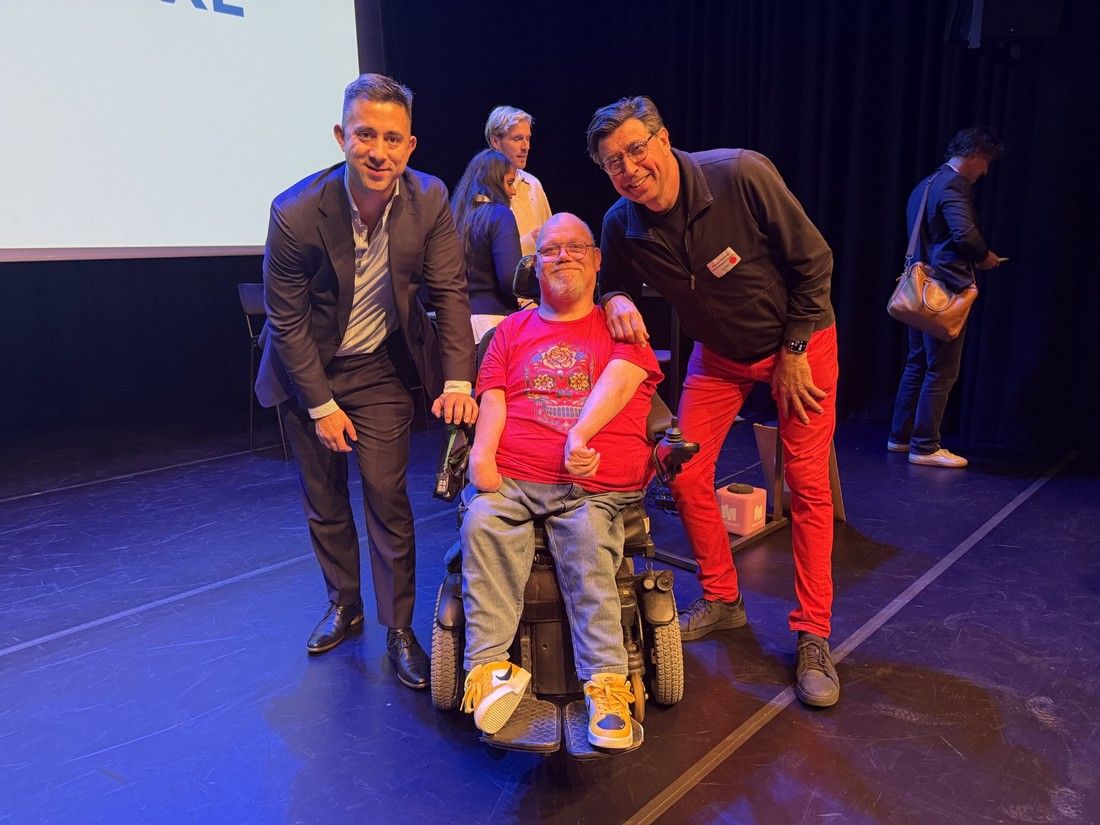 Op het podium staan van links naar rechts: wethouder Alexander Scholtes, Eric Groot Kormelink in zijn electrische rolstoel en Per van Bleijswijk. 