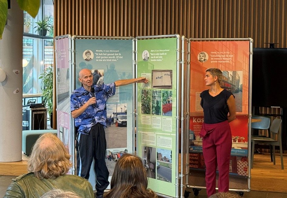 Albert en Odile van de Adviesraad LVB staan voor het kamerscherm in de zaal. Albert vertelt zijn verhaal. 